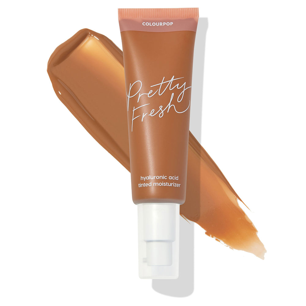 ColourPop Pretty Fresh Tinted Moisturizer in Dark 19 N stands upright with a white pump and blush-pink cap, a deep neutral caramel swatch behind; matte tan tube highlights the hyaluronic acid formula on a clean white background.