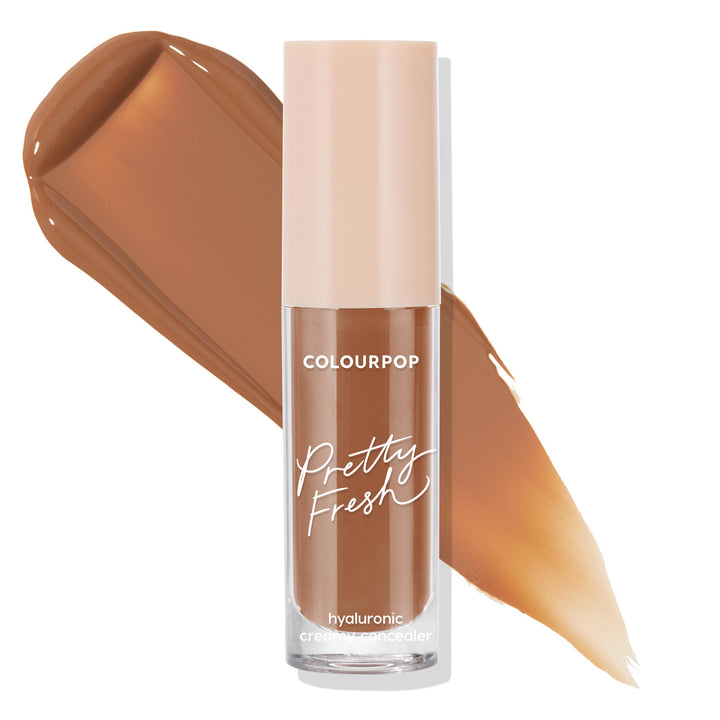 ColourPop Pretty Fresh Creamy Concealer Dark 180 N stands upright, showcasing a beige cap and clear tube with Pretty Fresh branding, while smooth deep neutral-brown hyaluronic formula swatches sweep behind on a white background.