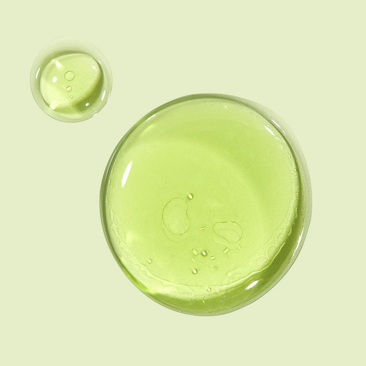 Avocado + Aloe Double Shot face serum forming glossy, translucent green drops that pool on a pale mint background, highlighting a lightweight, hydrating texture; ColourPop Face Serum.