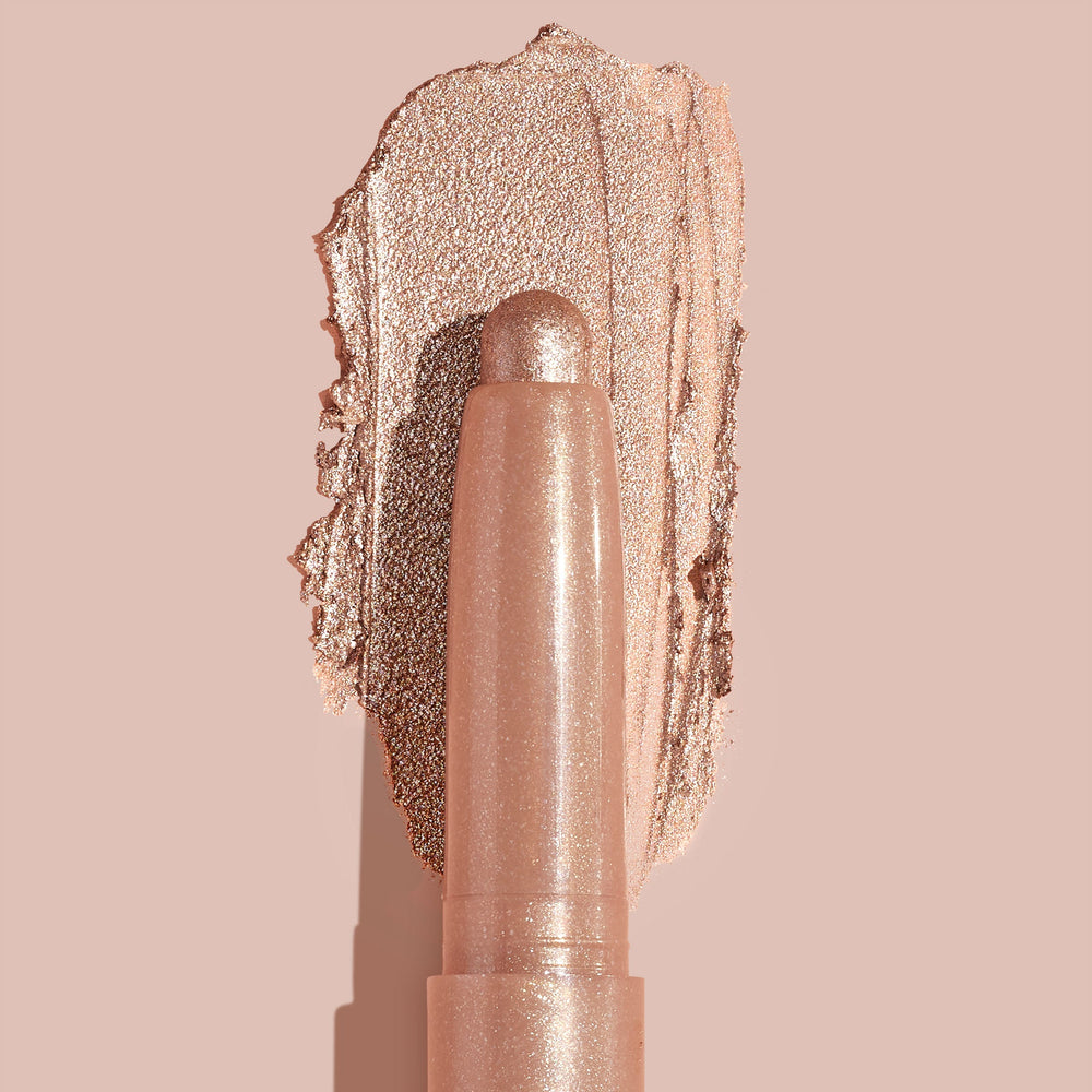Socialite ColourPop Shadow Stix glides a metallic champagne‑rose swipe across a nude backdrop, twist‑up cream eyeshadow stick shown close up to highlight smooth, blendable texture and high‑shine shimmer for quick eyelid application.