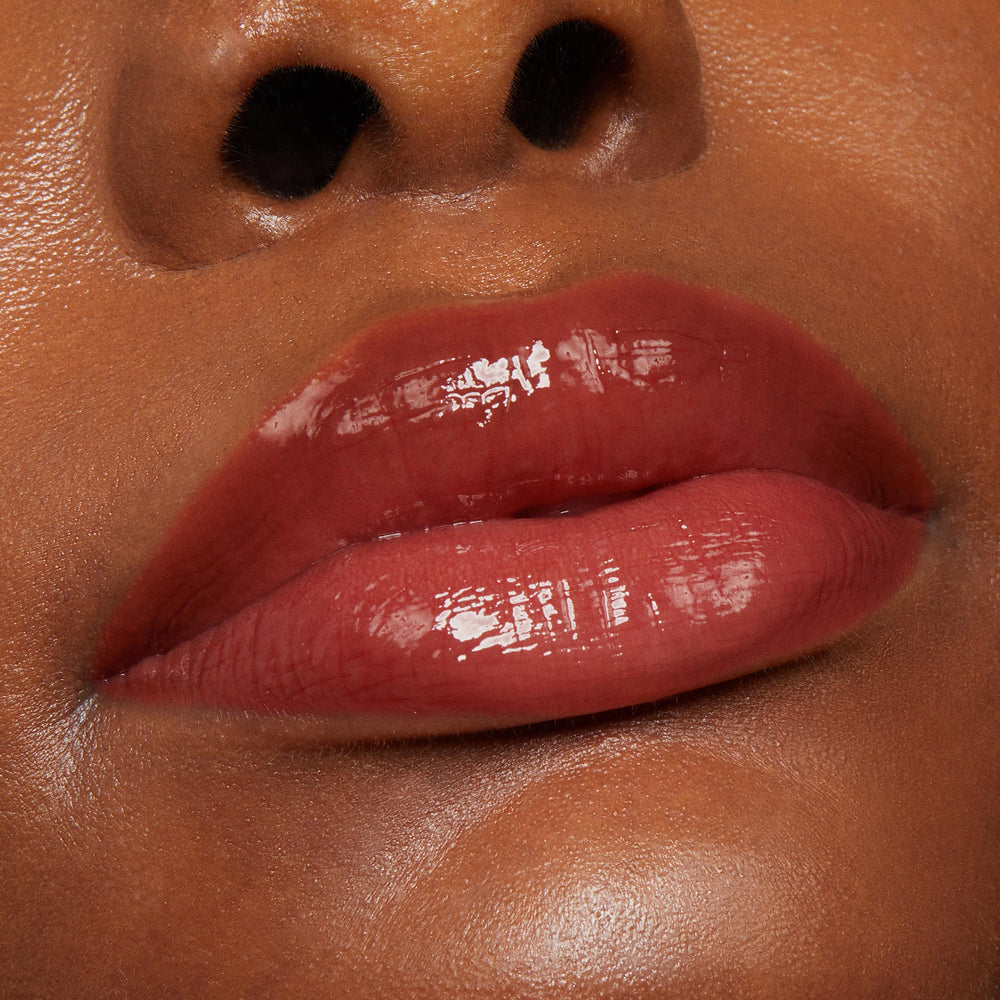 Glossy lips wear Vampy Lips Lux Lip Oil, a ColourPop Lux Lip Oil, in a tight beauty close-up, showing a rich berry-brown tint with high shine, smooth cushioned texture, and a hydrated finish against warm, even skin.
