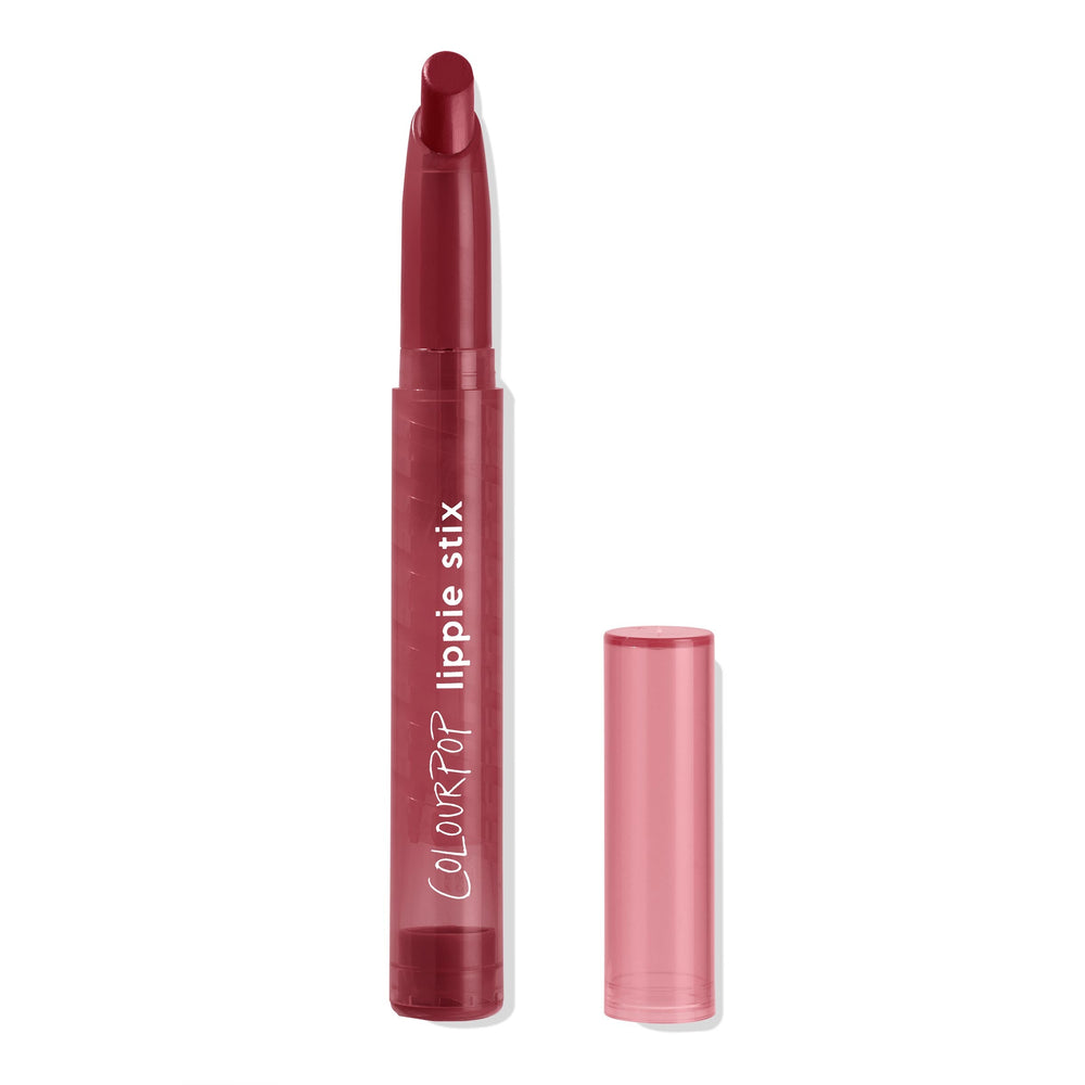 Bichette Lippie Stix by ColourPop standing uncapped, revealing a slim twist-up bullet in deep burgundy with an angled tip; transparent rosy cap beside the tube labeled “ColourPop lippie stix” on a white background.