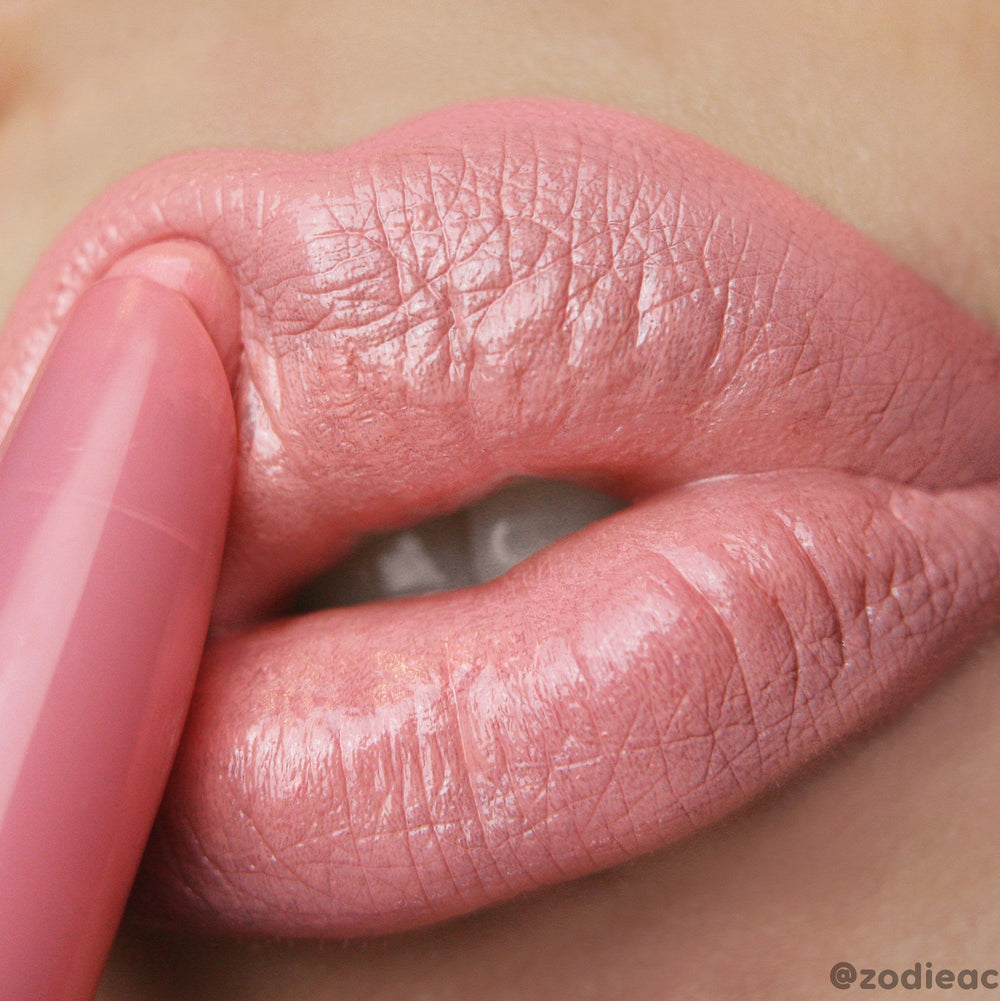 Caramella ColourPop Lippie Stix glides onto full lips, applying a creamy warm pink-peach nude with a glossy satin finish; extreme close-up macro shows the twist-up bullet and smooth, even coverage.
