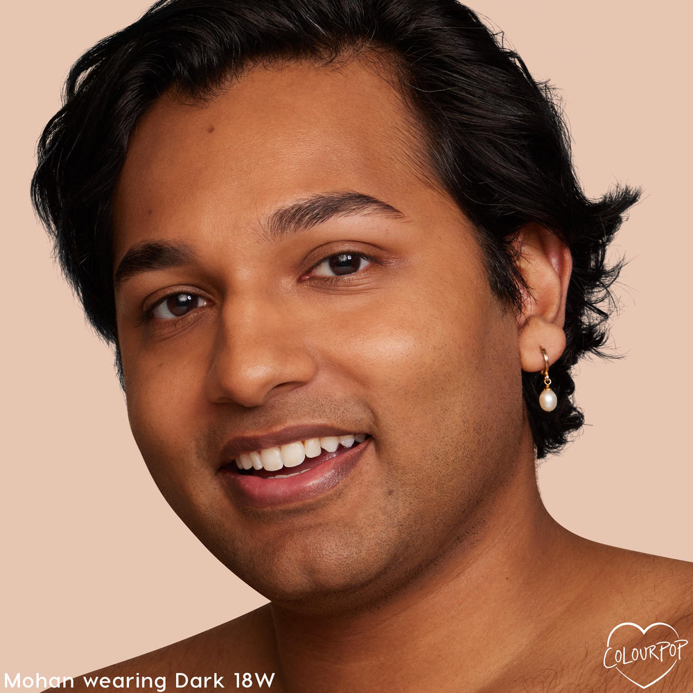 Model wearing ColourPop Pretty Fresh Tinted Moisturizer in Dark 18 W (warm), smiling in a close-up against a peach background, showcasing natural, dewy, even coverage and a skin-like finish.