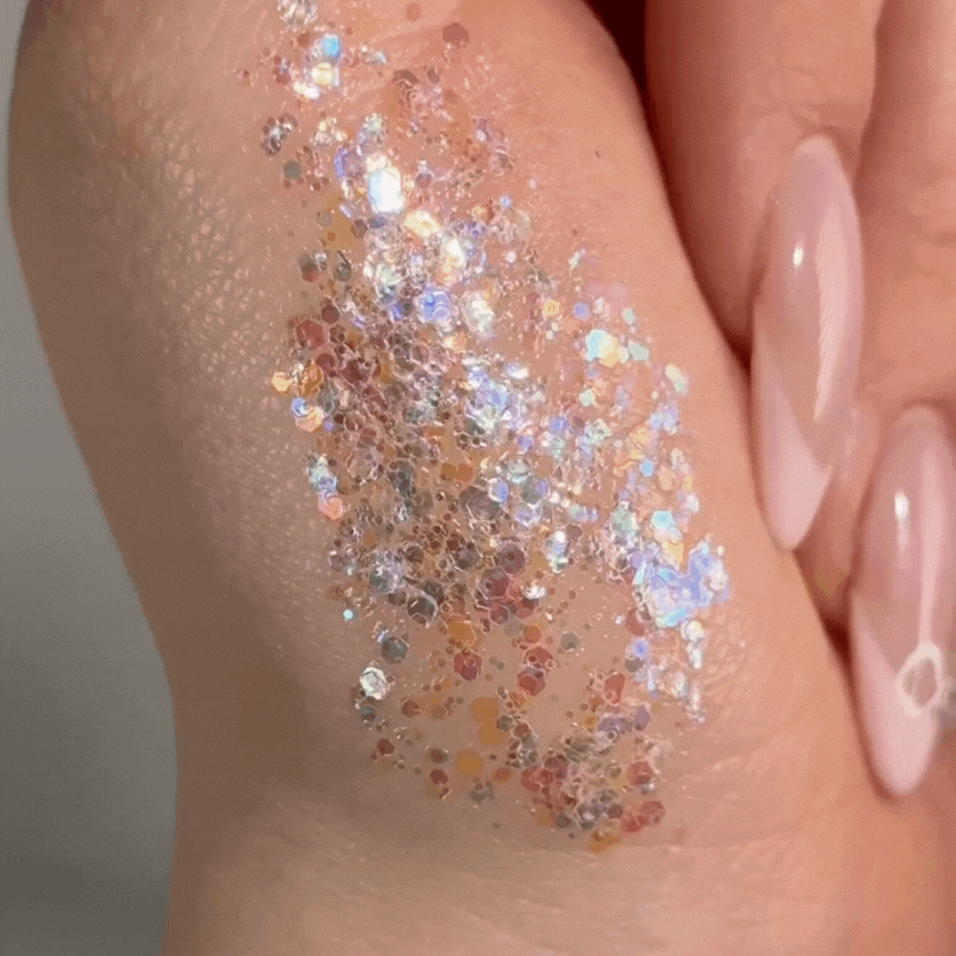 Disco Lady ColourPop Glitter Gel swatched on the back of a hand, shimmering with multicolor iridescent hex and micro-glitter in a clear gel base, catching light beside glossy nude-pink nails in a tight beauty close-up.