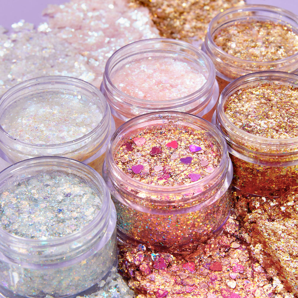 So Cute ColourPop Glitter Gel pots gleam open, showing iridescent white, rose, and gold glitter mixes with chunky flakes and pink heart confetti, swatched in glossy streaks on a pastel surface for bold eye and face sparkle.