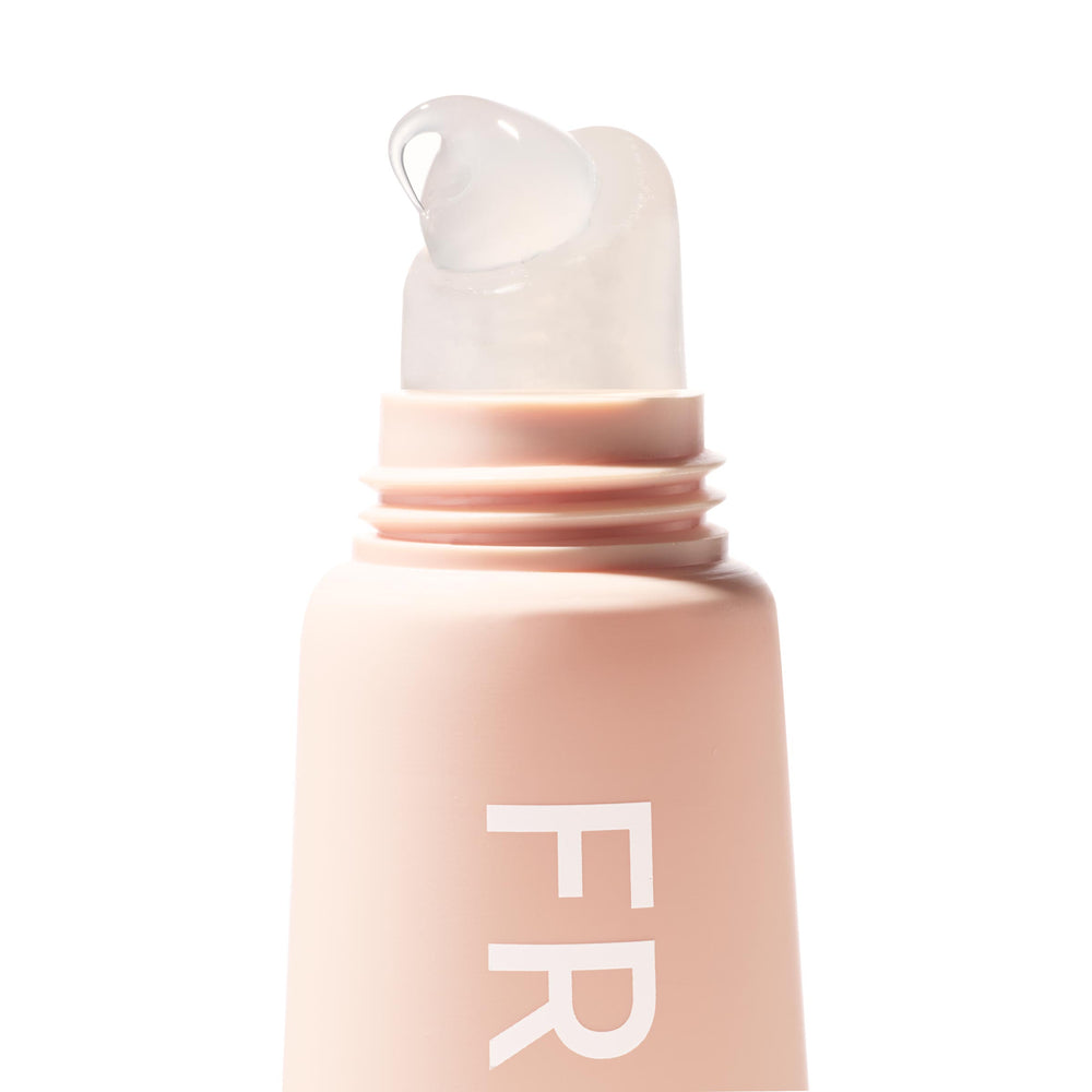 ColourPop Fresh Kiss Glossy Balm in Vanilla Cake dispensing a clear gloss bead from a slanted translucent applicator tip, shown in a macro close-up on a matte blush-pink tube against a clean white background.