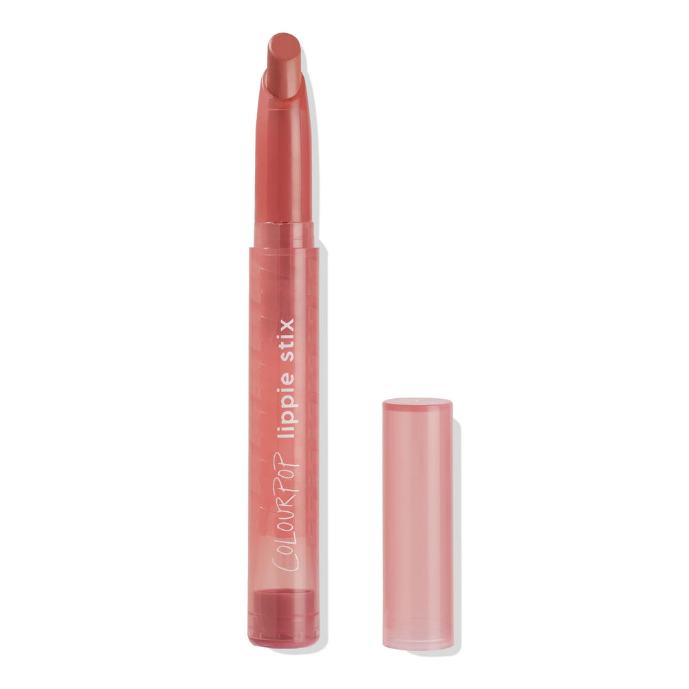ColourPop Lippie Stix NBD stands upright with cap placed beside it, slanted lipstick bullet extended in a warm rosy nude, housed in a translucent pink tube with white logo on a clean white background.