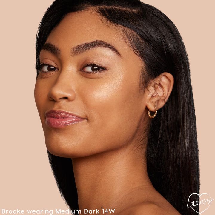 Model's face wearing Medium Dark 14 W, showcasing a natural, dewy finish from the ColourPop Pretty Fresh Tinted Moisturizer; soft glam with glossy lips and a small gold hoop earring against a nude background.