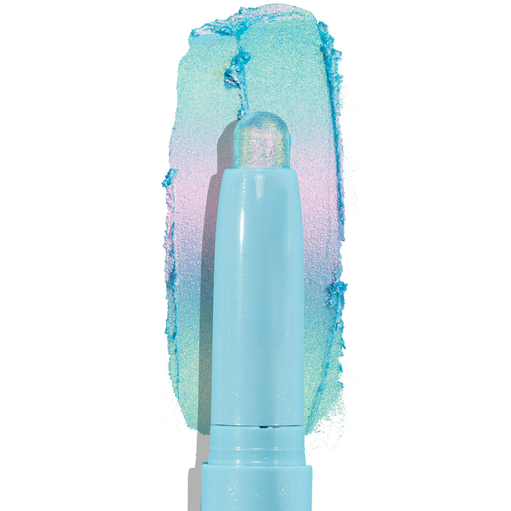 Colourpop Game Over Shadow Stix eye crayon gliding across a white background, leaving a bold metallic aqua, lavender, and mint duochrome shimmer swatch behind its pastel blue twist-up tube packaging.