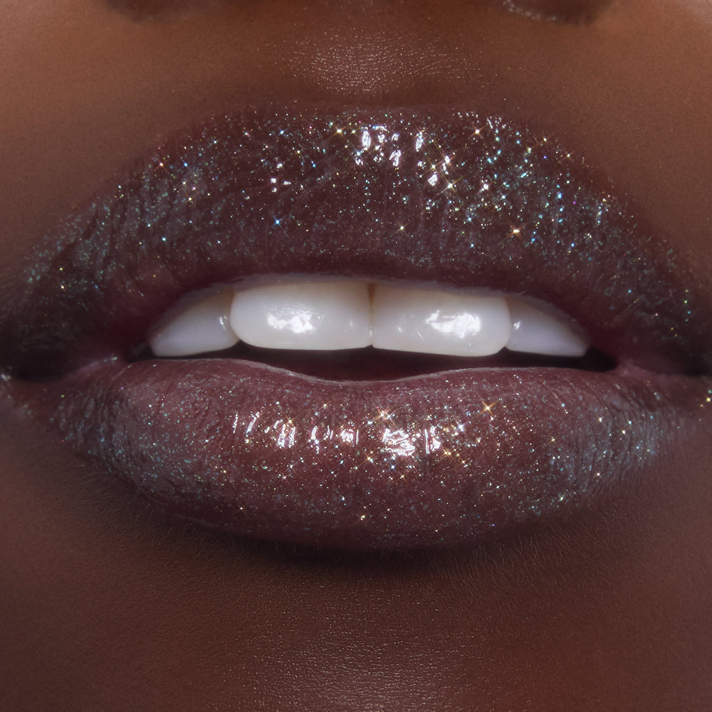 Shimmering lips wearing ColourPop Ultra Glossy Lip in Totally Swamped, a deep cool-toned gloss packed with multicolor sparkle, shown in an extreme close-up as the model parts their lips to reveal a high-shine, wet-look finish.