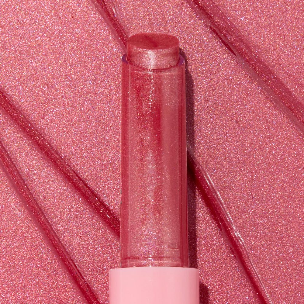 Shimmery rosy-pink Tini Time twist-up stick catches light, showcasing the glossy plumping payoff of the ColourPop So Juicy Plumping Gloss Balm with Peptides, set against swiped, glittery pink backdrop that emphasizes its glassy shine.
