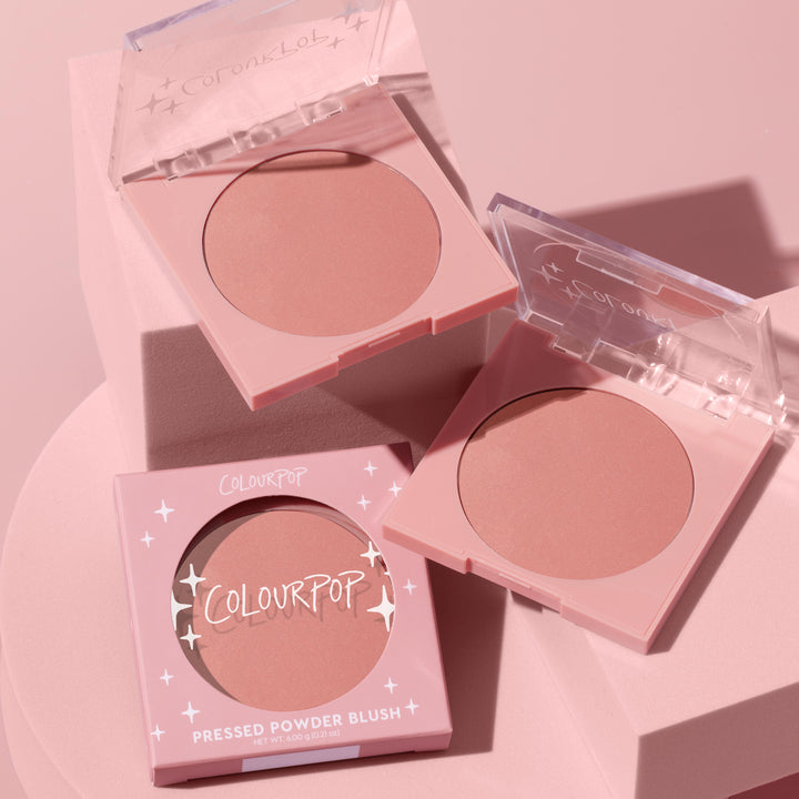 To the 10 ColourPop Pressed Powder Blush in pastel pink compacts, opened to show a soft rosy nude shade, styled with its boxed packaging on a pink pedestal under soft studio lighting, 6.0 g (0.21 oz) pan.