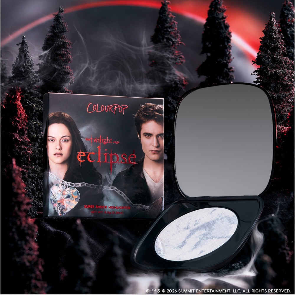 ColourPop Change Me Mega Highlighter compact lies open beside its Twilight Eclipse-themed box, featuring two characters, against a dark smoky forest and red eclipse sky for a dramatic, supernatural makeup product display.
