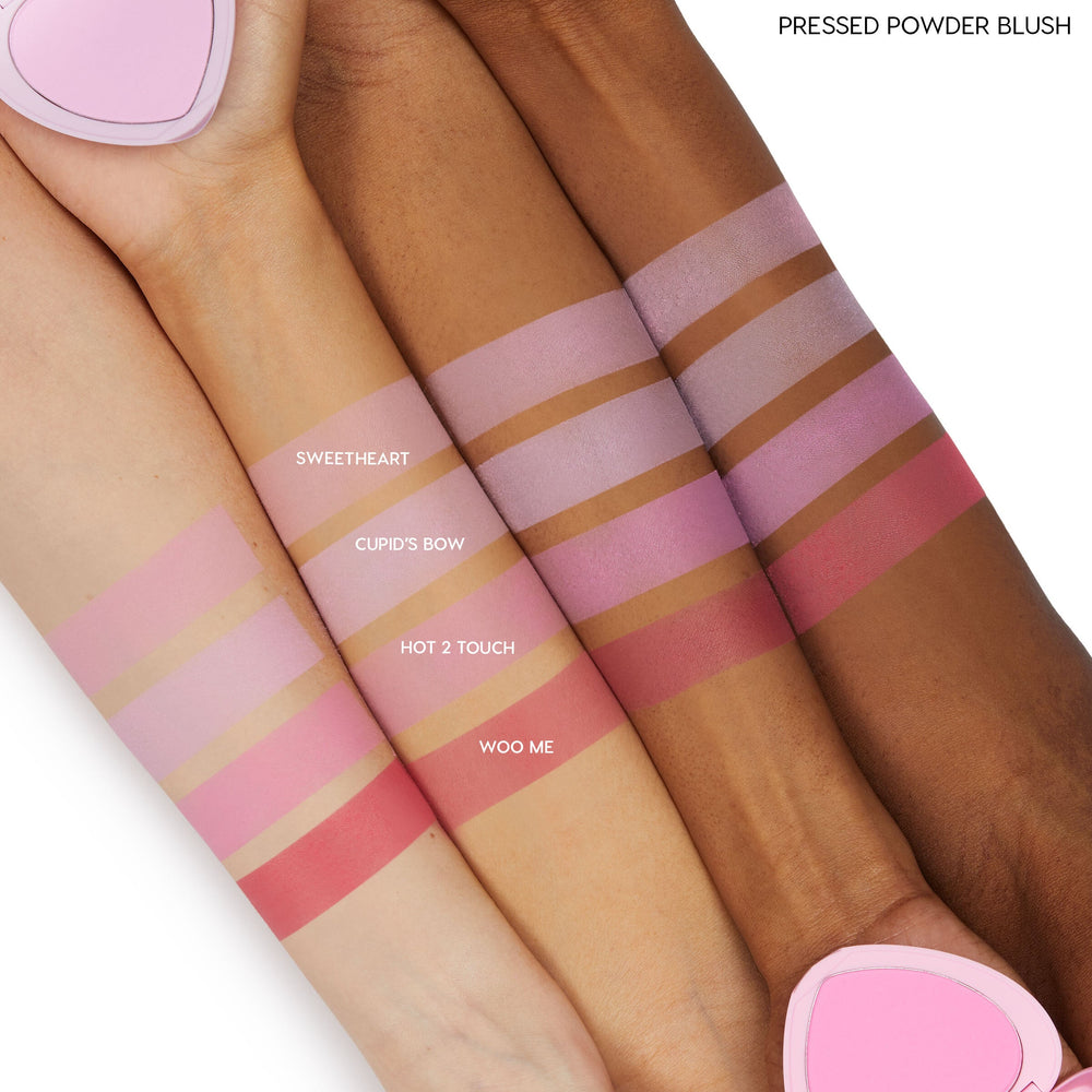 Woo Me pressed powder blush by ColourPop swatched on three arms, showing a rich rosy-pink stripe labeled “WOO ME” under Sweetheart, Cupid’s Bow, and Hot 2 Touch, demonstrating smooth pigment across light, medium, and deep skin tones.