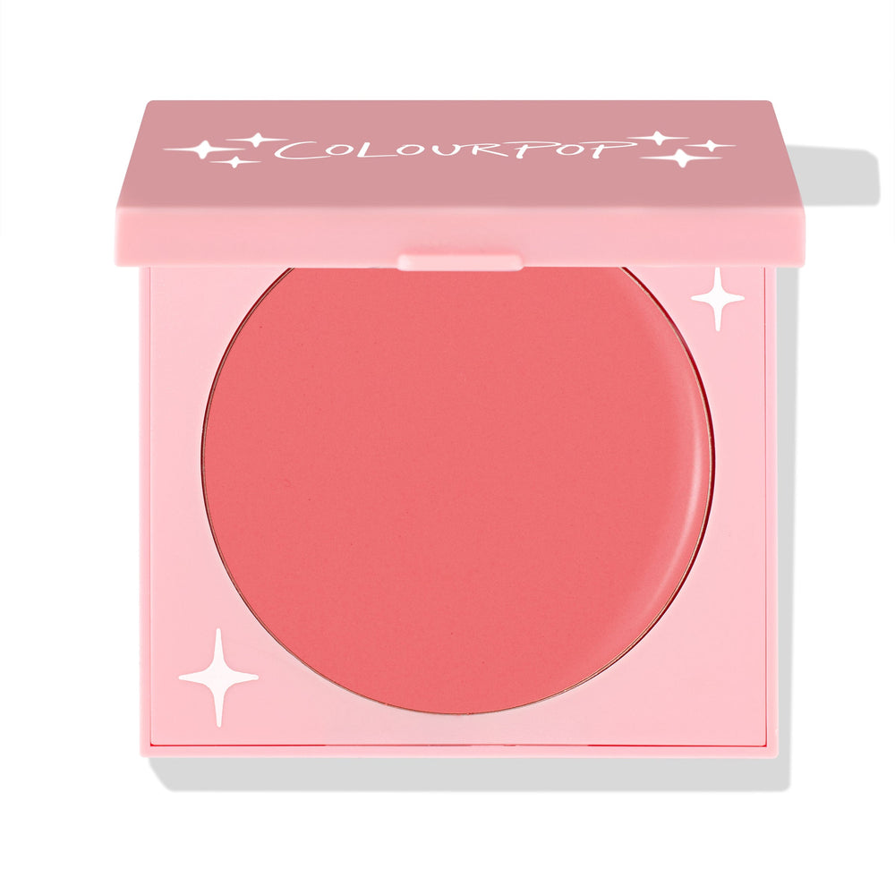 Whole Mood cream blush showing a warm coral shade as the pink compact with ColourPop logo sits half-open, revealing the round pan and star accents; studio close-up on white for ColourPop Cream Blush shoppers seeking a soft, natural flush.