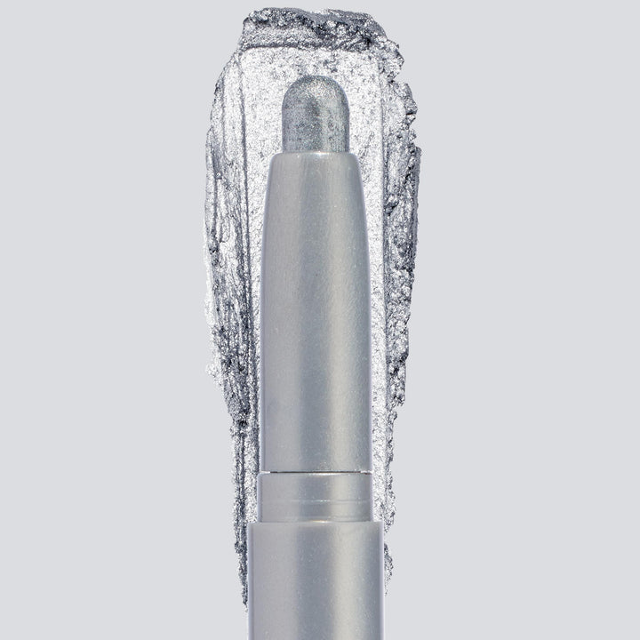 ColourPop Shadow Stix in Witch, Please showcases a creamy icy-silver shimmer, the crayon tip extended with a bold swatch behind to highlight pigment and sparkle, centered in a sleek silver tube on a light gray background.