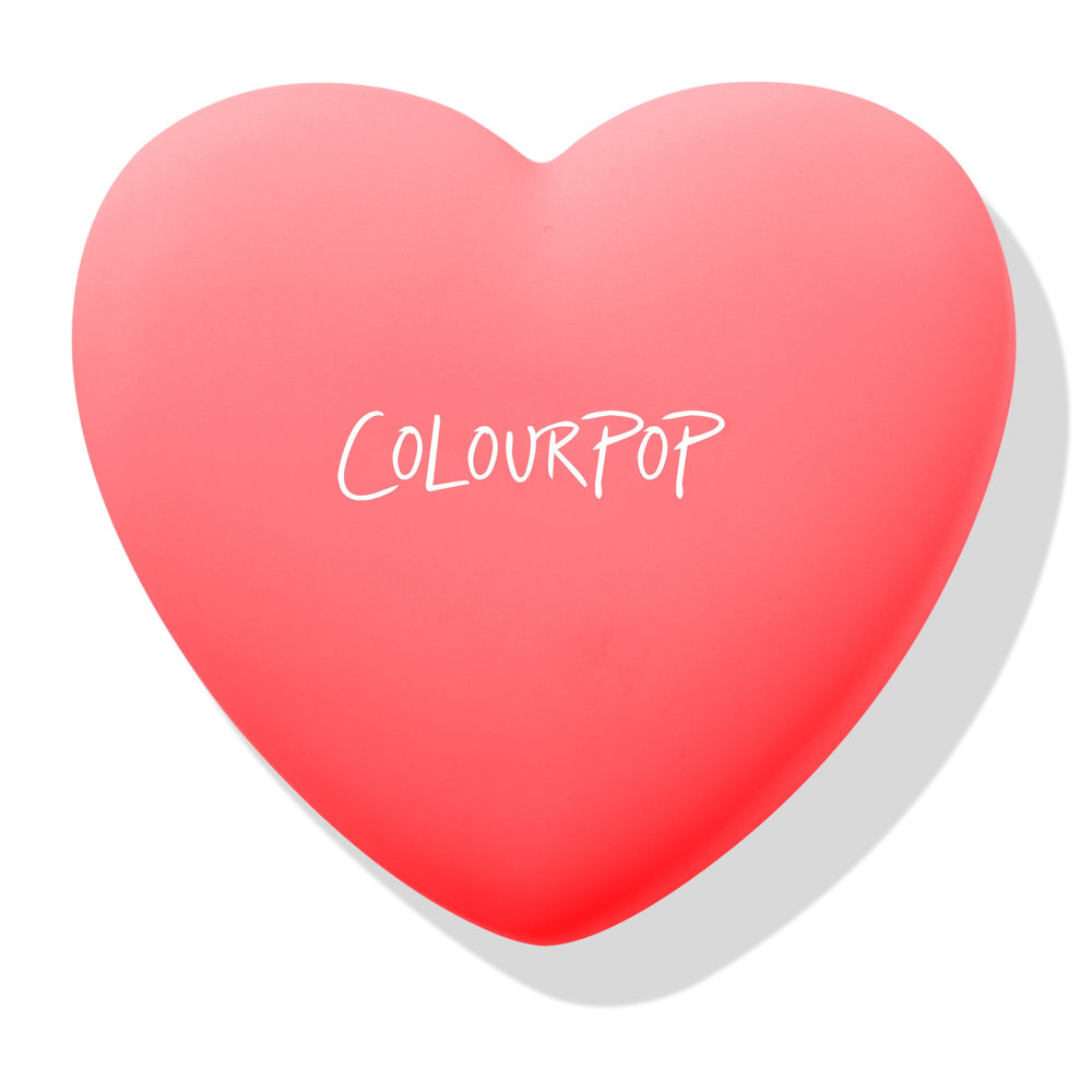 Heart-shaped coral compact shows the ColourPop logo, Woo Me pressed powder blush closed and ready to open, set on a white background with soft shadow; ColourPop Pressed Powder Blush in pink-red case.