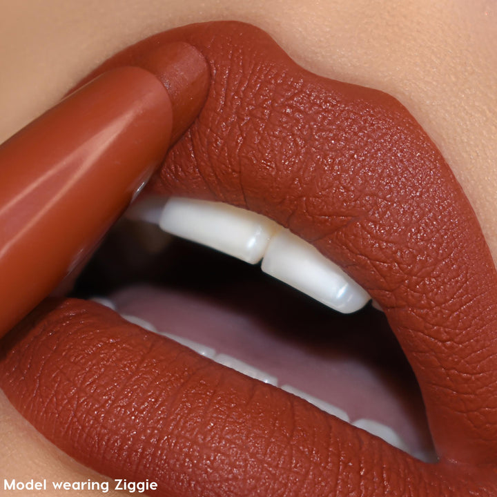 Ziggie ColourPop Lippie Stix coats lips as the bullet applies a warm terracotta brown, creating a soft-matte, full-coverage finish in a tight close-up, highlighting smooth texture and a precise lip line.