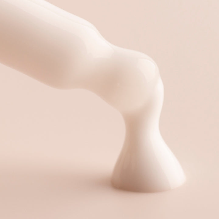 Coconut Face Milk, a ColourPop Face Milk, pours in a glossy white ribbon and pools on a soft beige surface, close-up emphasizing its lightweight, hydrating texture.