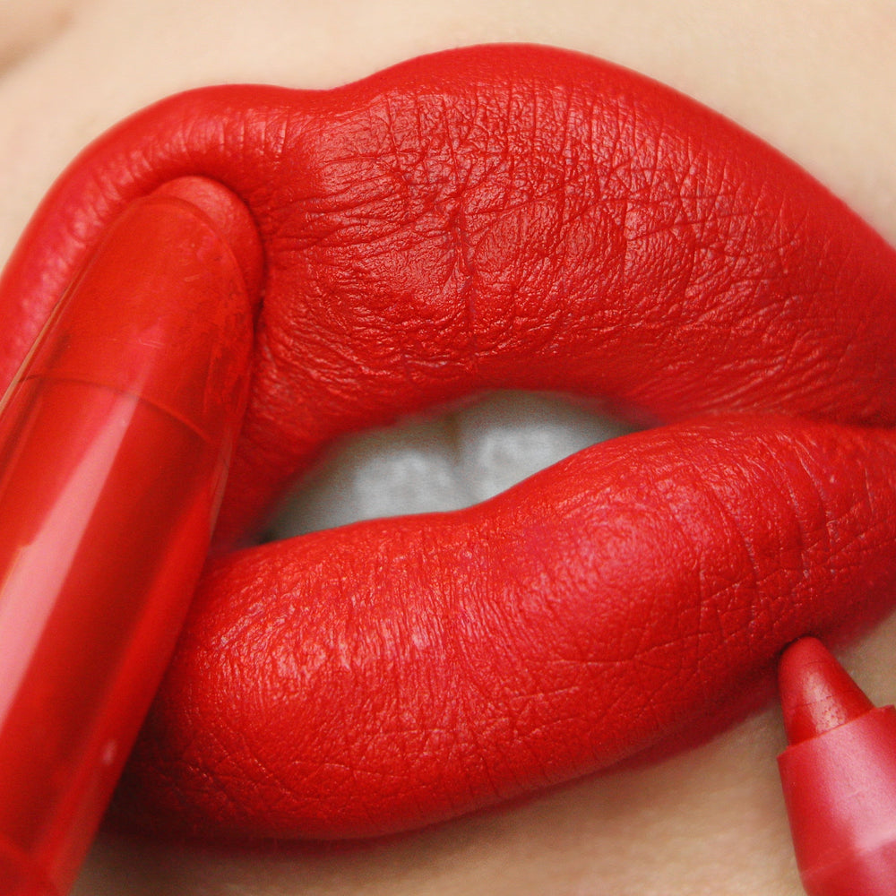 Bold red lips apply Trust Me, a ColourPop Lippie Stix, gliding on a matte true-red finish as the slim crayon tip and red tube define the lip line in an extreme close-up beauty shot.